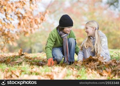 Two young children outdoors in park playing in leaves and smiling (selective focus)