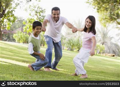Two young children outdoors in park pulling smiling father by arms (selective focus)