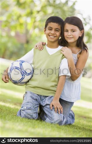 Two young children outdoors in park with ball smiling (selective focus)