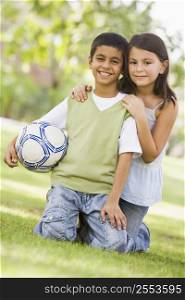 Two young children outdoors in park with ball smiling (selective focus)