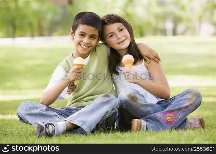 Two young children outdoors in park with ice cream smiling (selective focus)