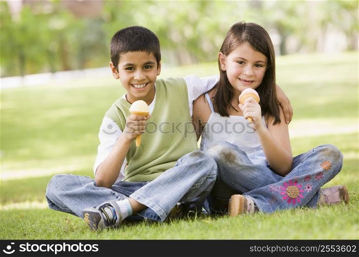 Two young children outdoors in park with ice cream smiling (selective focus)