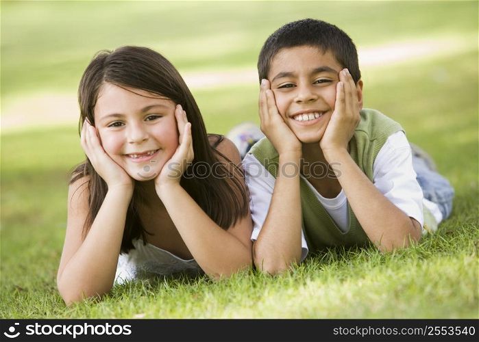 Two young children outdoors lying in park smiling (selective focus)