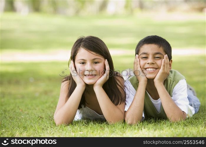 Two young children outdoors lying in park smiling (selective focus)