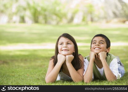 Two young children outdoors lying in park smiling (selective focus)