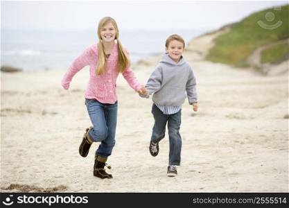 Two young children running on beach holding hands smiling