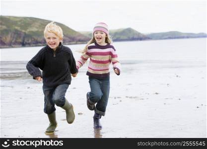 Two young children running on beach holding hands smiling