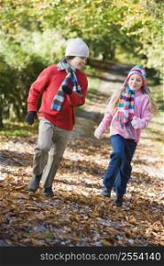 Two young children running on path outdoors smiling (selective focus)