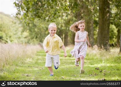 Two young children running on path smiling