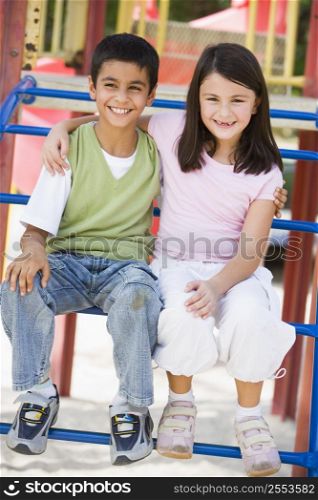 Two young children sitting on playground structure smiling (selective focus)