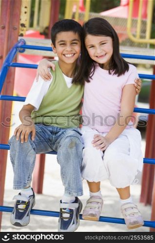 Two young children sitting on playground structure smiling (selective focus)