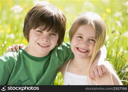 Two young children sitting outdoors arm in arm smiling