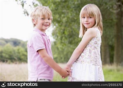 Two young children standing outdoors holding hands smiling