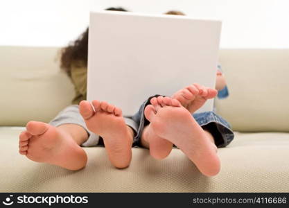 Two young children surfing the wold wide web on a laptop while sitting on a settee