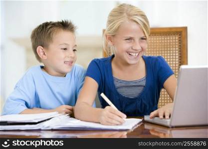 Two young children with laptop doing homework in dining room smiling