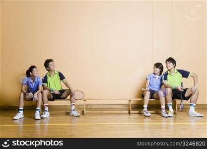 Two young couples sitting on a bench and holding badminton rackets