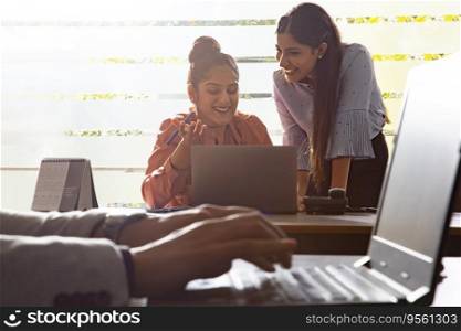 TWO YOUNG EXECUTIVES LOOKING AT LAPTOP AND HAPPILY DISCUSSING WORK IN OFFICE