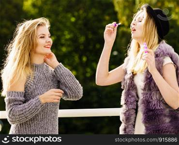 Two young fashion women best friends having fun together blowing bubbles with toy bubble wand while enjoying sunny day outdoors. Happiness and carefree concept.. Women blowing soap bubbles, having fun