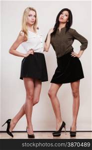 Two young fashion women caucasian and african in trendy short black skirts posing in full length studio portrait