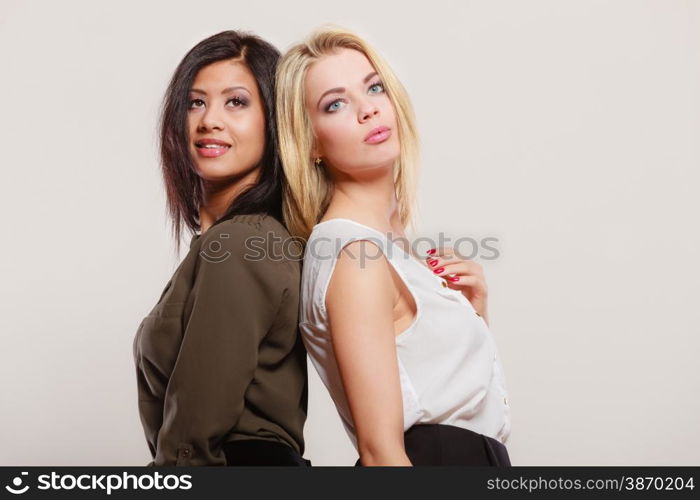 Two young fashionable women caucasian and african posing studio portrait on gray