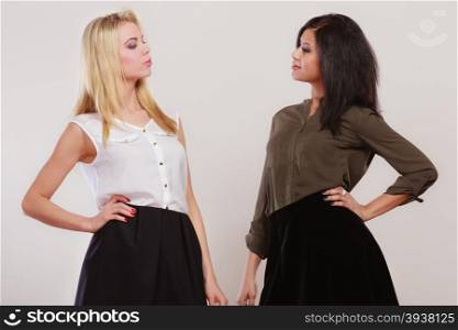 Two young fashionable women caucasian and african posing studio portrait on gray