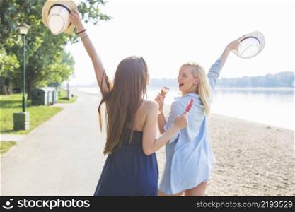 two young female friend holding hat enjoying icecream beach