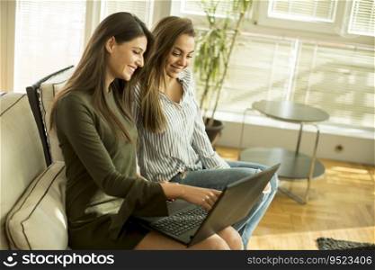Two young female friends sitting in a room on the sofa and using laptop