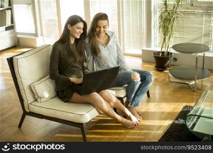 Two young female friends sitting in a room on the sofa and using laptop