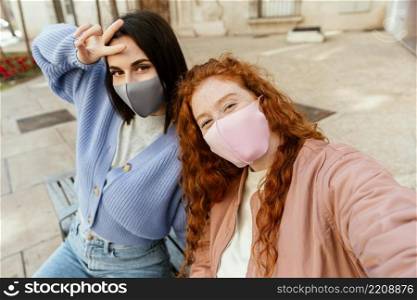 two young female friends with face masks outdoors taking selfie