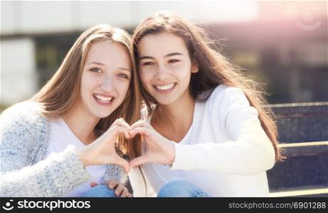 Two Young Female Teenagers Holding Hands in the Shape of a Heart and Smiling, Looking at the Camera