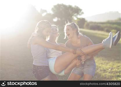 Two young females fooling around trying to carry friend