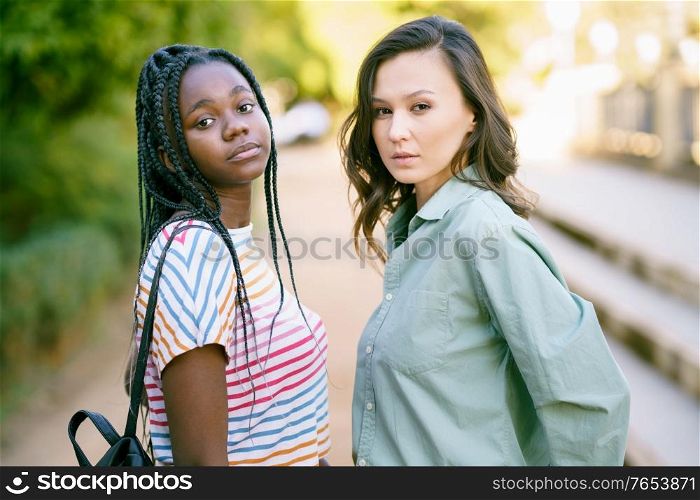 Two young friends looking at camera together on the street. Multiethnic women.. Two Multiethnic women looking at camera together on the street.