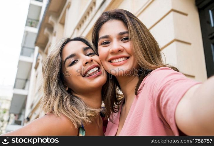 Two young friends smiling and taking a selfie together while standing outdoors. Urban concept.