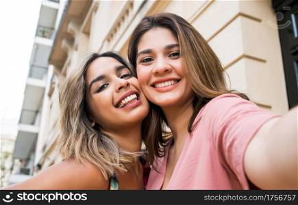 Two young friends smiling and taking a selfie together while standing outdoors. Urban concept.