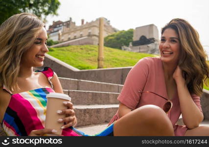 Two young friends spending time together and talking while sitting on stairs outdoors. Urban concept.