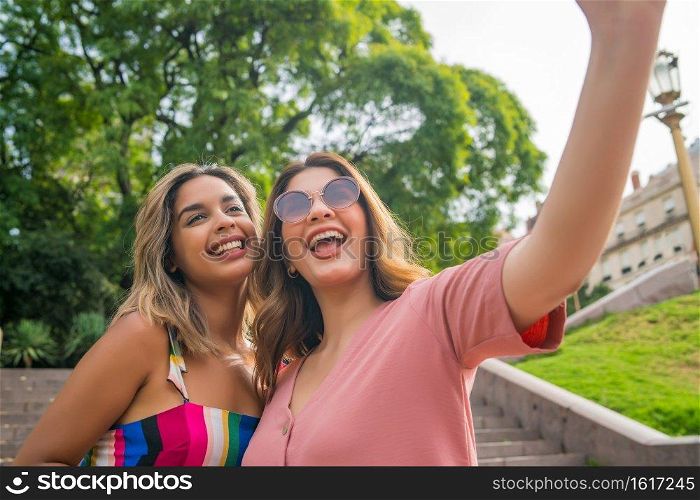 Two young friends taking a selfie and smiling while standing outdoors. Urban concept.