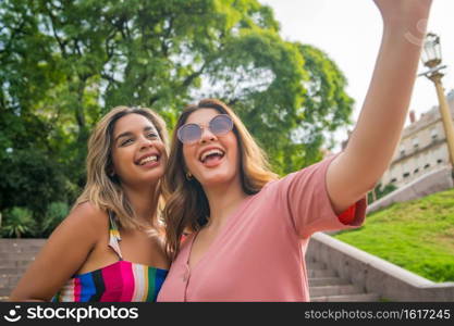 Two young friends taking a selfie and smiling while standing outdoors. Urban concept.