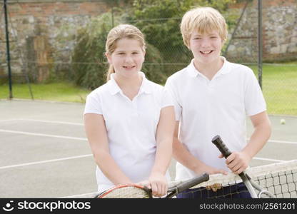 Two young friends with rackets on tennis court smiling