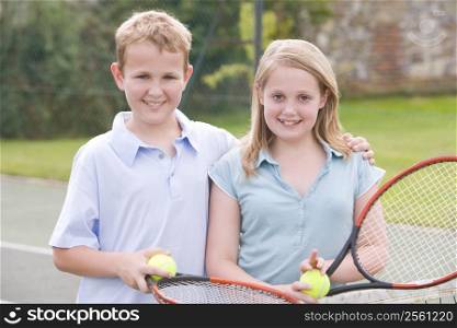 Two young friends with rackets on tennis court smiling