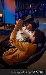 Two young gamers having fun in video game club. Virtual entertainment, e-sport tournament, cybersport lifestyle. Male person leisures in internet cafe. Two young gamers having fun in game club