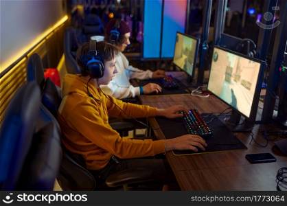 Two young gamers in headsets play in video game club. Virtual entertainment, e-sport tournament, cybersport lifestyle. Male person leisures in internet cafe. Two young gamers in headsets play in video game club