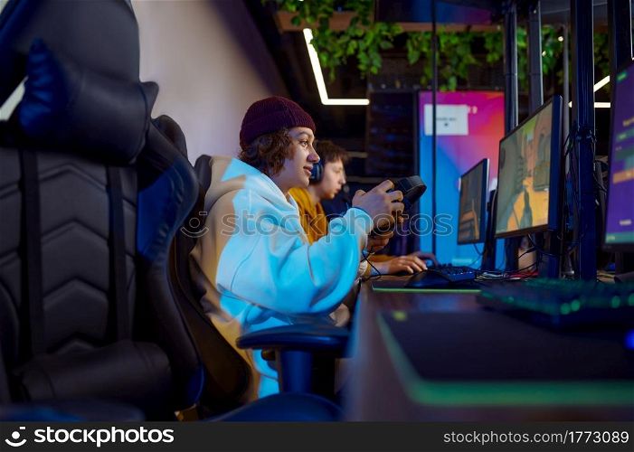 Two young gamers play in video game club. Virtual entertainment, e-sport tournament, cybersport lifestyle. Male person leisures in internet cafe. Two young gamers play in game club