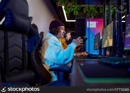 Two young gamers play in video game club. Virtual entertainment, e-sport tournament, cybersport lifestyle. Male person leisures in internet cafe. Two young gamers play in game club
