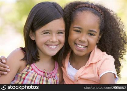 Two young girl friends sitting outdoors smiling