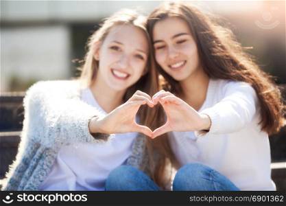Two Young Girlfriends Holding Hands in the Shape of a Heart and Smiling, Looking at the Camera