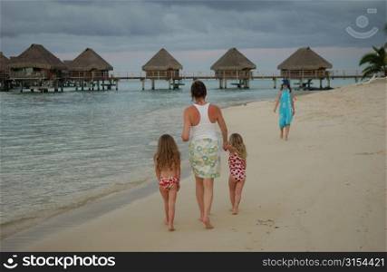 Two young girls (6-8) walking on a beach with their mother, Moorea, Tahiti, French Polynesia, South Pacific