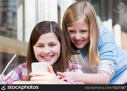Two Young Girls At Cafe Reading Text Message On Mobile Phone