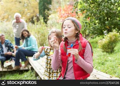 Two Young Girls Blowing Bubbles On Countryside Picnic