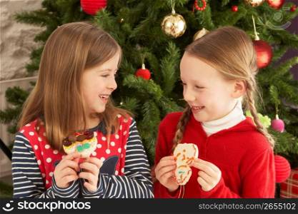 Two Young Girls Eating Cookies In Front Of Christmas Tree