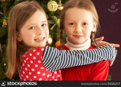Two Young Girls Hugging In Front Of Christmas Tree